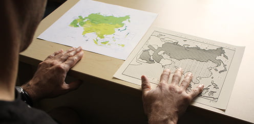 Image of man sitting at desk with a printed map comparing a tactile graphic of the same map produced by T-Base.