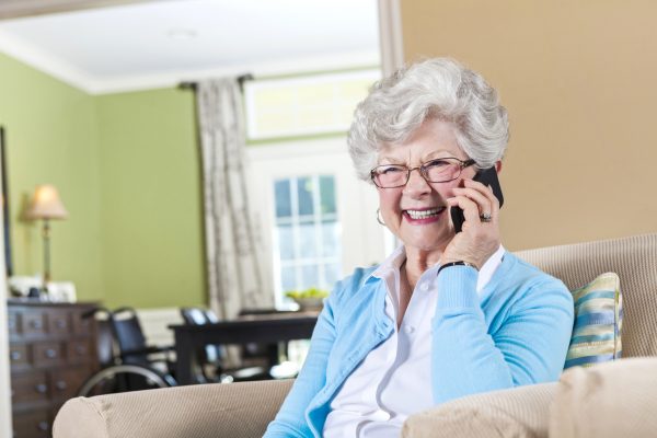 Image of senior woman in a living room, smiling while talking on the telephone, depicting a satisfied subscriber.